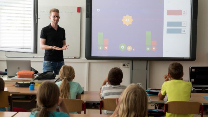 Leraar staat naast digibord voor kinderen in een klaslokaal