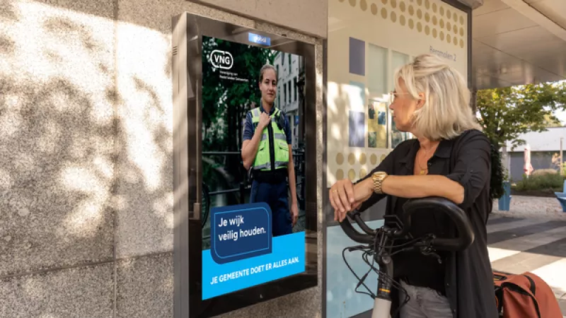 Vrouw kijkt naar abri met daarin poster van campagne VNG