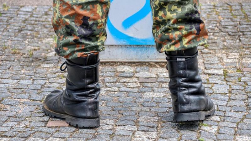 voeten en onderste deel benen van een soldaat, zichtbaar zijn de schoenen en de camouflagebroek, straatstenen op de achtergrond