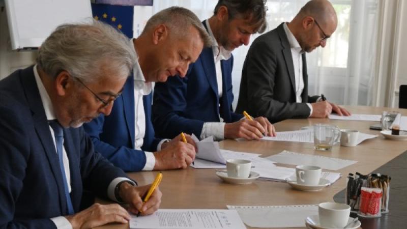 Vier mannen aan tafel zetten tegelijk hun handtekening