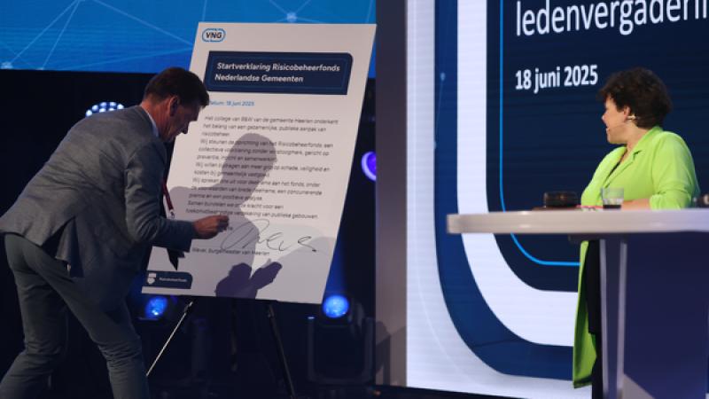 Roel Wever zet op het podium zijn handtekening onder de tekst op een groot bord, Sharon Dijksma kijkt toe