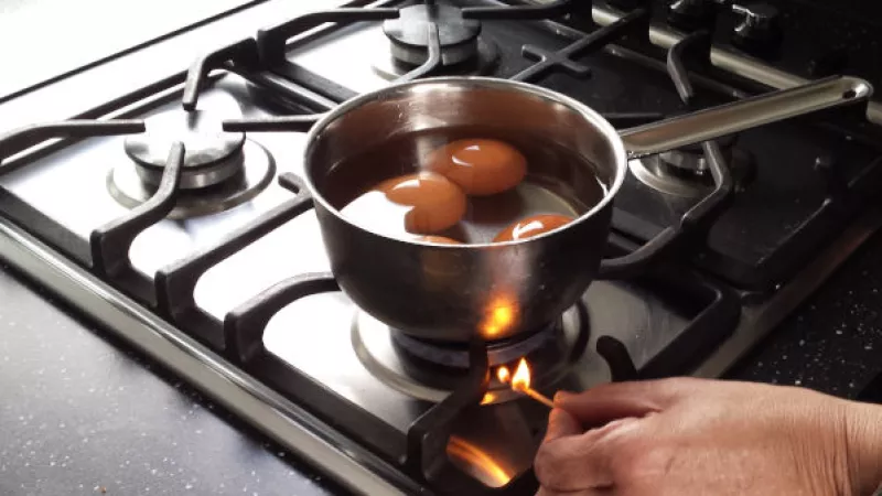 Close-up van hand die gas aansteekt onder een pan met eieren