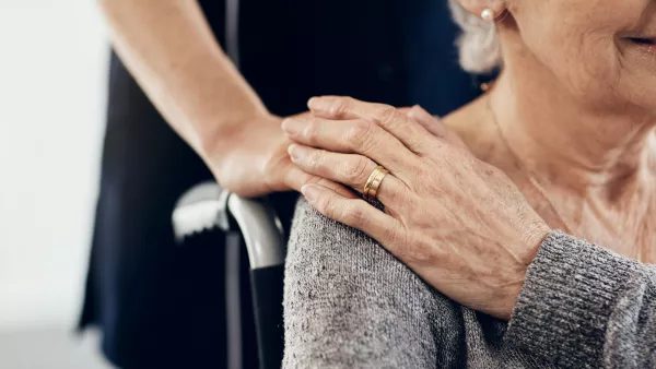 vrouw legt haar hand op de schouder van een oudere vrouw in een rolstoel