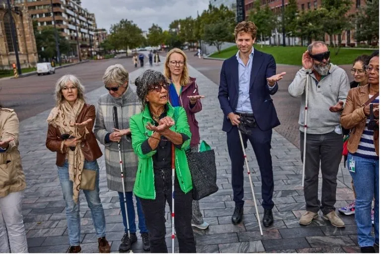 Joan Titarsolej op straat in Rotterdam met een groepje mensen, Joan en een aantal mensen dragen een geleidestok