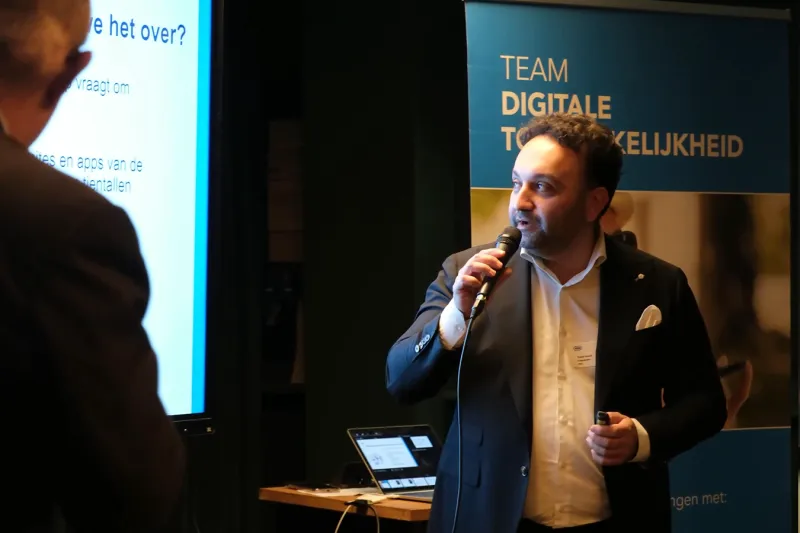 Projectleider Yousuf Yousufi presenteert op het podium tijdens een Raadsledenbijeenkomst over Digitale Toegankelijkheid.